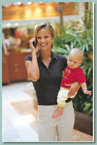 Mother carrying baby and talking on cell phone.